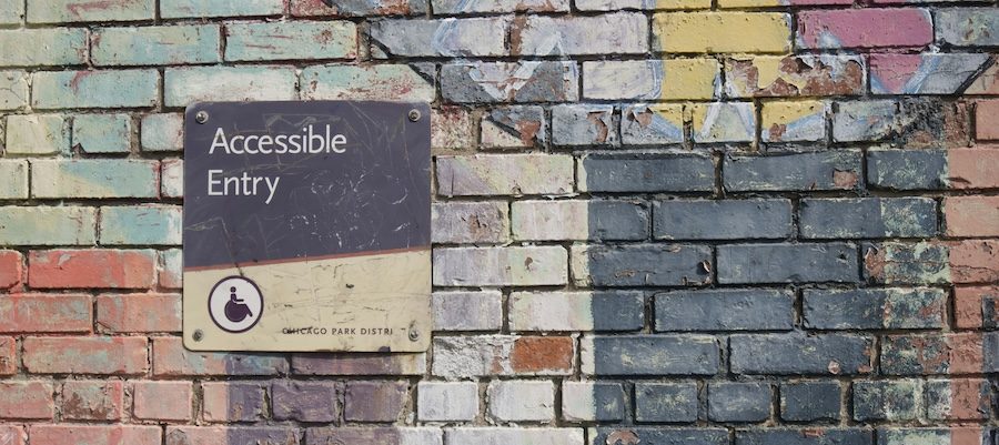 Brick wall with an accessible entry sign on it.