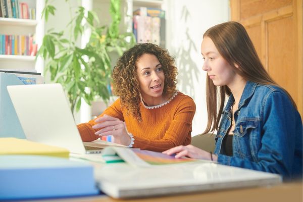 Advisor works at laptop with college student in a bright, comfortable environment